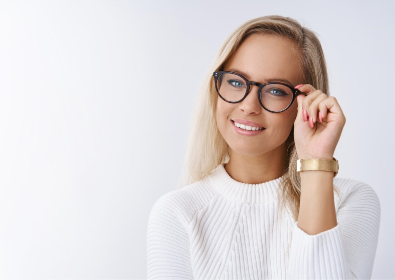 A young blonde woman wearing glasses and a sweater, looking elegant and sophisticated.