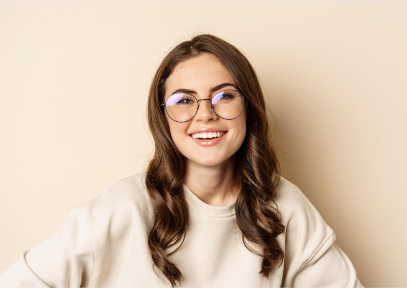 A young woman with a bright smile wearing clear eyeglasses on a beige background